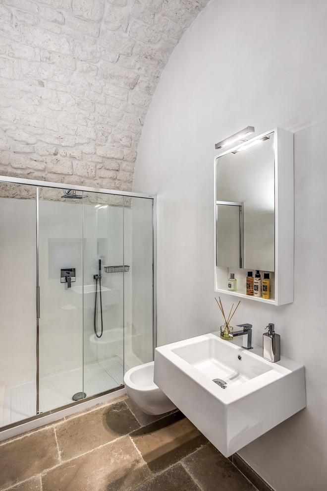 Ejemplo de cuarto de baño mediterráneo con ducha empotrada, sanitario de pared, paredes blancas, lavabo suspendido, suelo marrón y ducha con puerta corredera