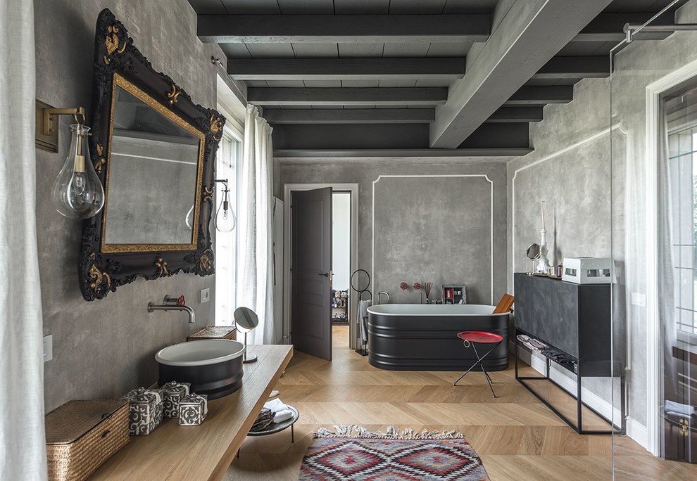 Industrial Badezimmer mit freistehender Badewanne, grauen Fliesen, grauer Wandfarbe, braunem Holzboden, Aufsatzwaschbecken, Waschtisch aus Holz, beigem Boden und beiger Waschtischplatte in Mailand