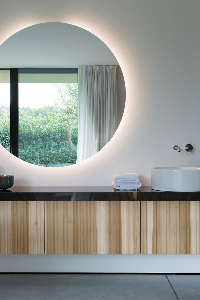 Idée de décoration pour une salle de bain minimaliste en bois clair avec un placard à porte plane, un mur blanc, une vasque, un sol gris et un plan de toilette noir.