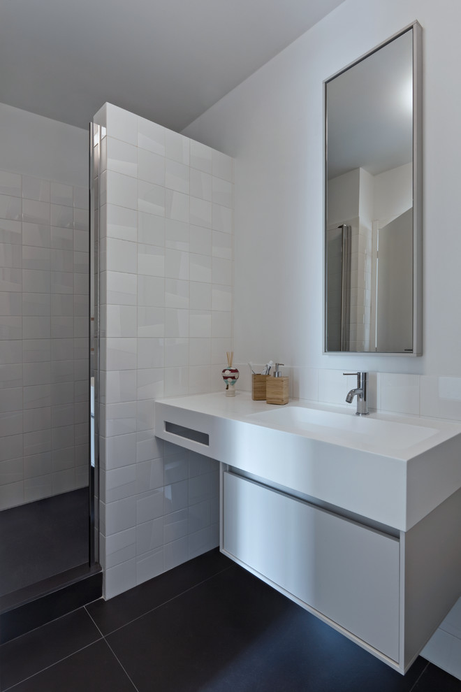 На фото: маленькая ванная комната в современном стиле с белыми фасадами, душем в нише, раздельным унитазом, белой плиткой, керамической плиткой, белыми стенами, полом из керамогранита, душевой кабиной, монолитной раковиной, столешницей из искусственного кварца, черным полом, душем с распашными дверями и белой столешницей для на участке и в саду