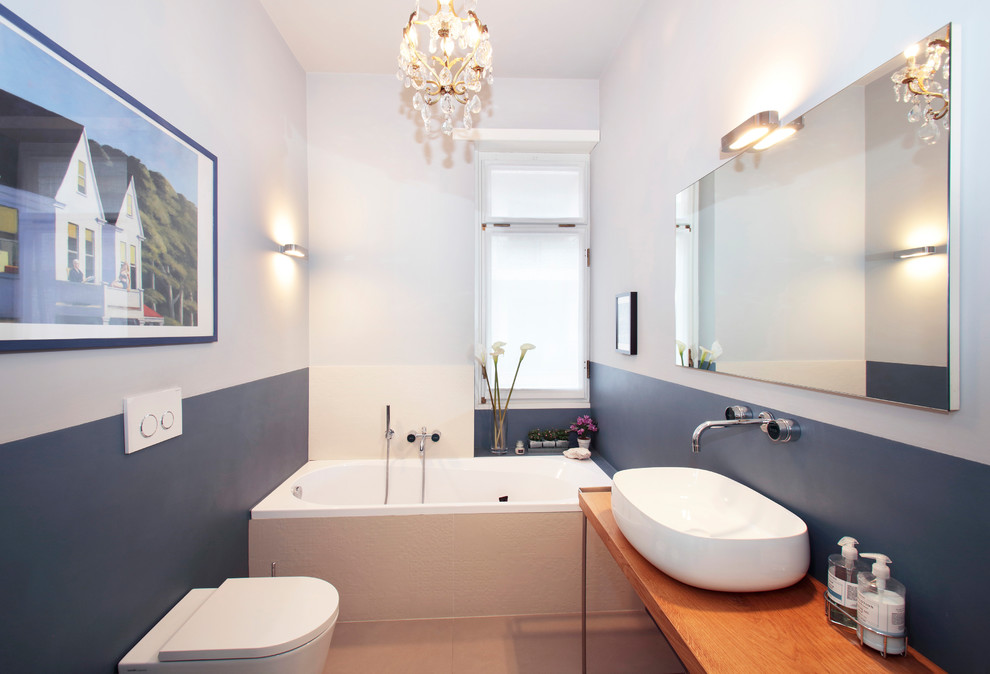 Cette photo montre une petite salle d'eau tendance avec un placard à porte plane, une baignoire posée, WC suspendus, un mur gris, une vasque, un plan de toilette en bois, un sol beige et un plan de toilette marron.