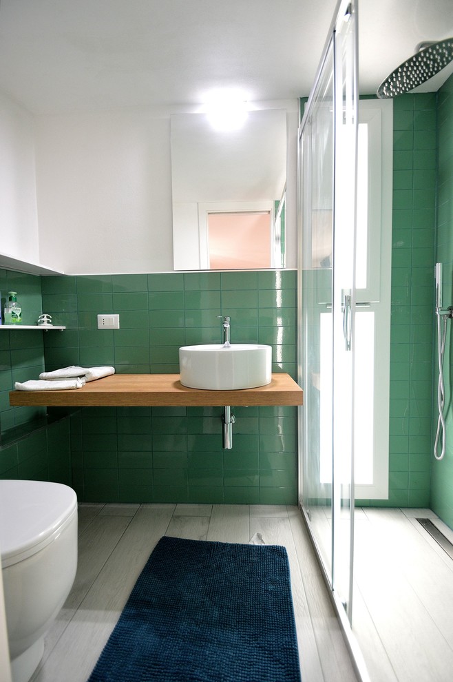Свежая идея для дизайна: маленькая ванная комната в стиле модернизм с открытыми фасадами, светлыми деревянными фасадами, душем без бортиков, унитазом-моноблоком, зеленой плиткой, керамической плиткой, белыми стенами, полом из керамогранита, душевой кабиной, настольной раковиной, столешницей из дерева, белым полом, душем с раздвижными дверями и коричневой столешницей для на участке и в саду - отличное фото интерьера