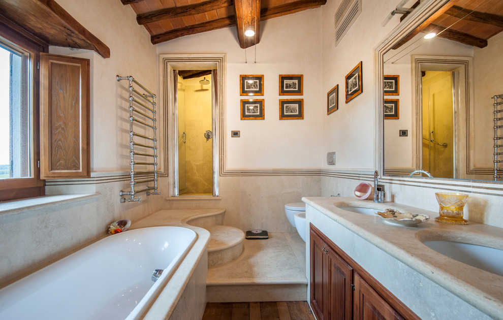 Country ensuite bathroom in Florence with raised-panel cabinets, dark wood cabinets, a built-in bath, an alcove shower, a wall mounted toilet, beige walls, dark hardwood flooring, a submerged sink, concrete worktops, brown floors, a hinged door and grey worktops.