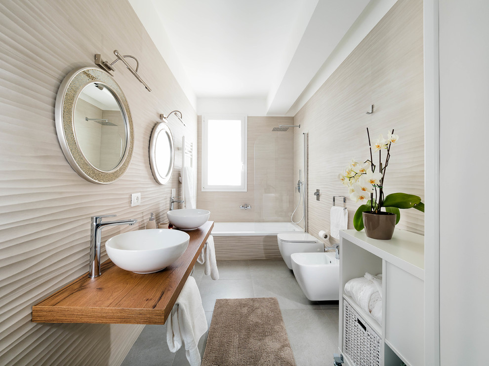 Inredning av ett brun brunt badrum med dusch, med ett badkar i en alkov, en dusch/badkar-kombination, en bidé, beige kakel, beige väggar, ett fristående handfat, träbänkskiva, grått golv och dusch med gångjärnsdörr