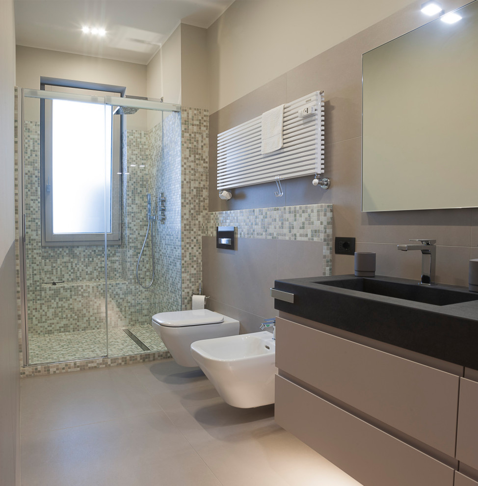 Пример оригинального дизайна: ванная комната среднего размера в современном стиле с плоскими фасадами, серыми фасадами, душем в нише, инсталляцией, серой плиткой, керамогранитной плиткой, серыми стенами, полом из керамогранита, душевой кабиной, монолитной раковиной, серым полом, черной столешницей, тумбой под две раковины, подвесной тумбой, сиденьем для душа, душем с раздвижными дверями, многоуровневым потолком и столешницей из искусственного кварца