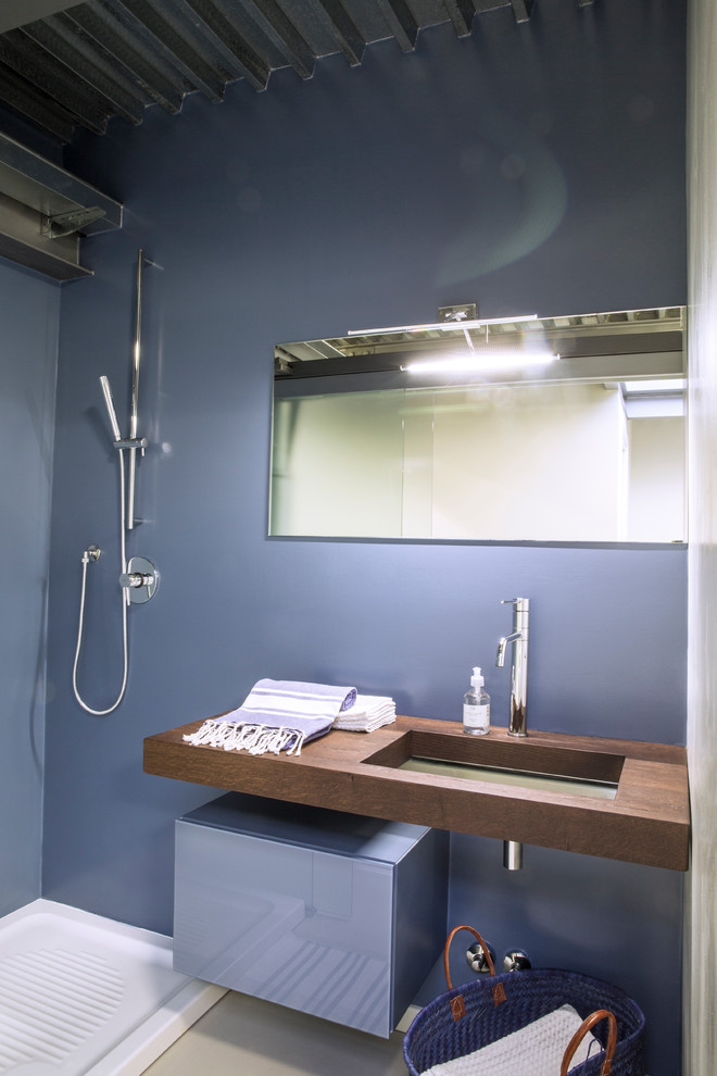 Exempel på ett mellanstort industriellt badrum med dusch, med luckor med glaspanel, blå skåp, en öppen dusch, en vägghängd toalettstol, blå väggar, betonggolv, ett undermonterad handfat, träbänkskiva, vitt golv och dusch med skjutdörr