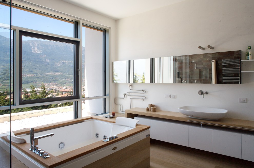 Modelo de cuarto de baño principal grande con jacuzzi, lavabo sobreencimera, encimera de madera, paredes blancas, suelo de madera clara y suelo beige