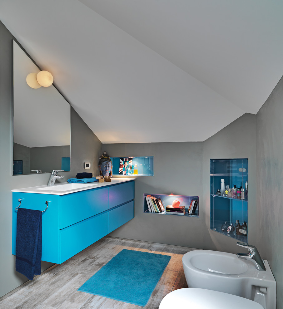 Ejemplo de cuarto de baño principal moderno pequeño con armarios con paneles lisos, puertas de armario azules, bidé, baldosas y/o azulejos grises, paredes grises, suelo de baldosas de porcelana, lavabo integrado y encimera de acrílico