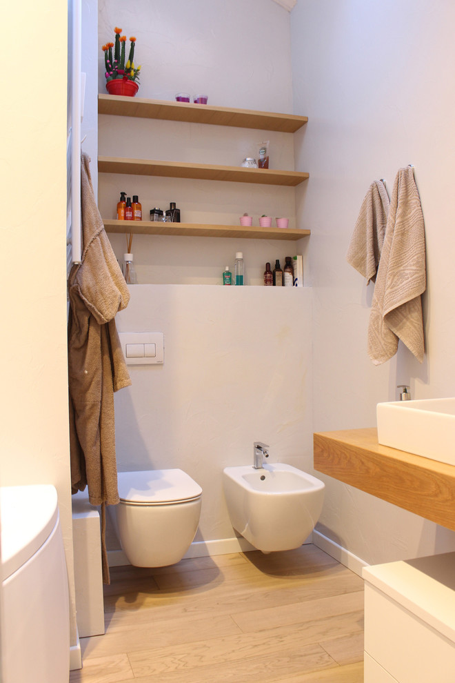 На фото: главная ванная комната среднего размера в современном стиле с открытыми фасадами, светлыми деревянными фасадами, угловой ванной, инсталляцией, серыми стенами, деревянным полом, раковиной с несколькими смесителями и столешницей из дерева