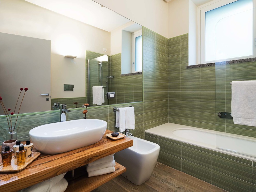 Bild på ett mellanstort funkis brun brunt en-suite badrum, med öppna hyllor, skåp i mellenmörkt trä, ett platsbyggt badkar, en bidé, grön kakel, gröna väggar, ett fristående handfat, träbänkskiva, en dusch/badkar-kombination, mörkt trägolv, brunt golv och med dusch som är öppen