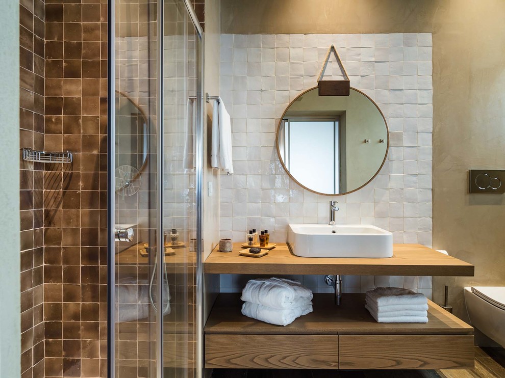 Contemporary shower room bathroom in Other with open cabinets, medium wood cabinets, white tiles, brown tiles, wooden worktops, a sliding door, a corner shower, a wall mounted toilet, brown walls, a vessel sink and brown worktops.