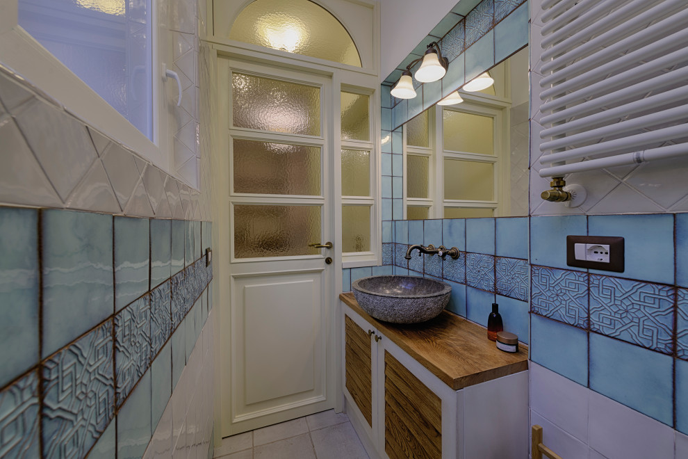 На фото: ванная комната среднего размера в средиземноморском стиле с фасадами с филенкой типа жалюзи, бежевыми фасадами, открытым душем, унитазом-моноблоком, разноцветной плиткой, керамической плиткой, разноцветными стенами, полом из керамической плитки, душевой кабиной, настольной раковиной, столешницей из дерева, бежевым полом, душем с раздвижными дверями, коричневой столешницей, тумбой под одну раковину и напольной тумбой