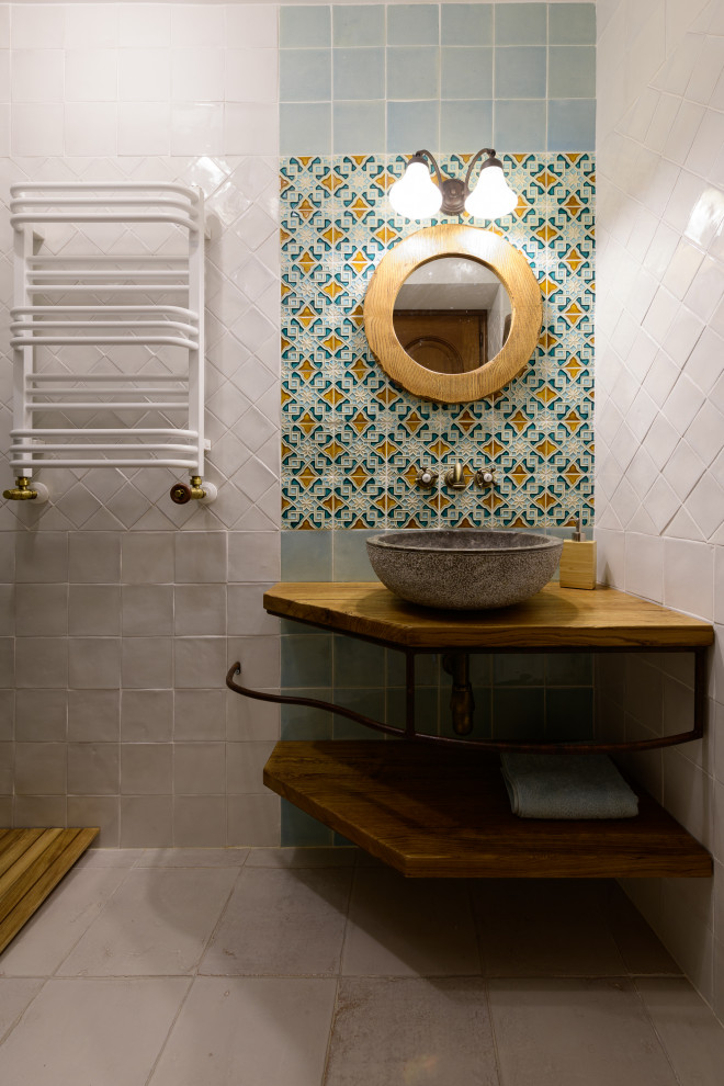 На фото: ванная комната среднего размера в средиземноморском стиле с фасадами с филенкой типа жалюзи, бежевыми фасадами, открытым душем, унитазом-моноблоком, разноцветной плиткой, керамической плиткой, разноцветными стенами, полом из керамической плитки, душевой кабиной, настольной раковиной, столешницей из дерева, бежевым полом, душем с раздвижными дверями, коричневой столешницей, тумбой под одну раковину и напольной тумбой с