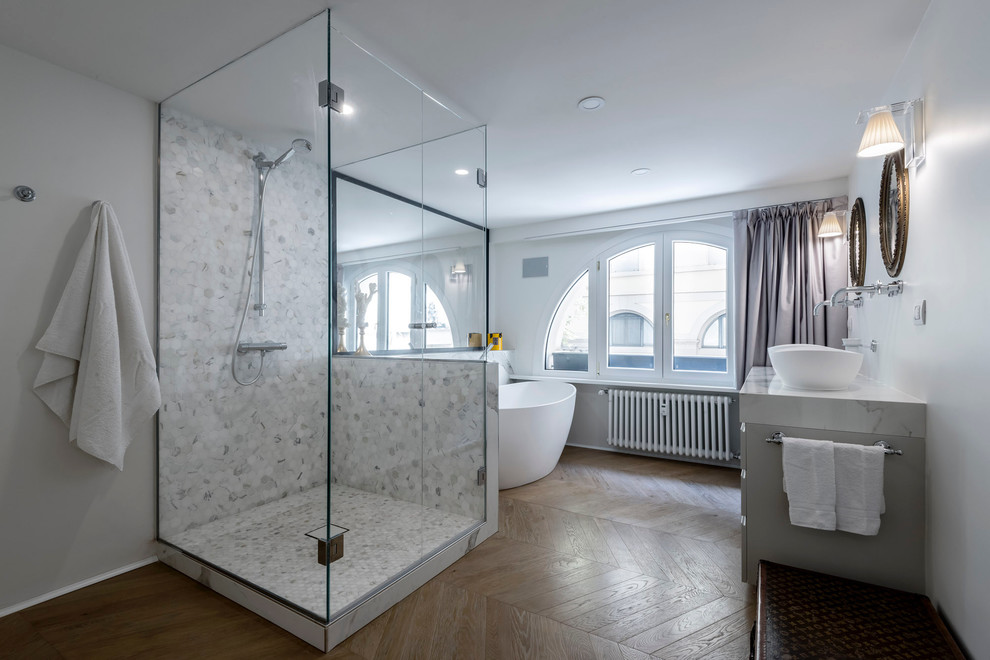 Foto på ett stort funkis en-suite badrum, med ett fristående badkar, vita väggar, mellanmörkt trägolv, ett fristående handfat, brunt golv, dusch med gångjärnsdörr, grå skåp, flerfärgad kakel och marmorbänkskiva
