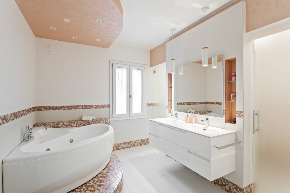 Photo of a large modern bathroom in Other with flat-panel cabinets, white cabinets, a corner bath, a bidet, multi-coloured tiles, mosaic tiles, porcelain flooring, a built-in sink, solid surface worktops, white floors and white worktops.