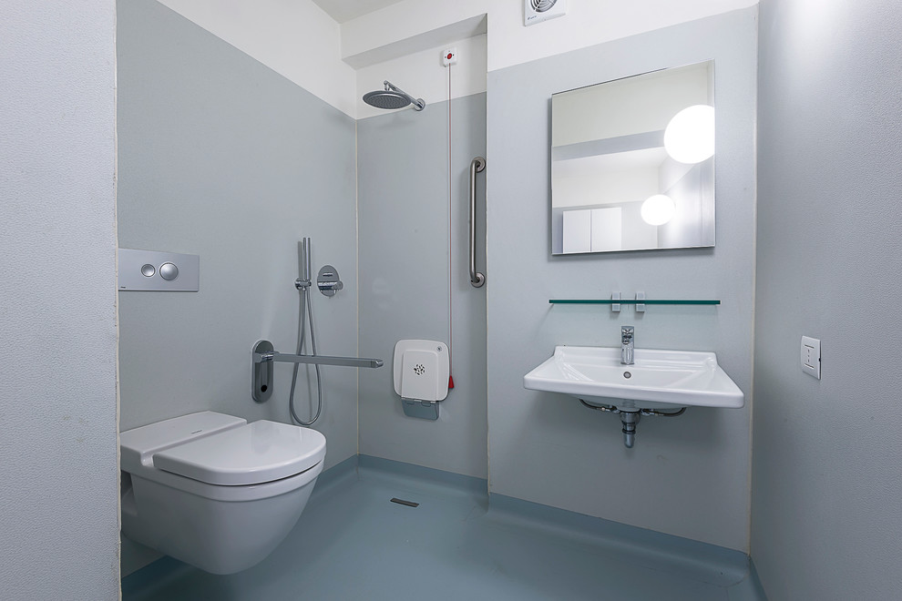 Modern inredning av ett litet badrum med dusch, med en öppen dusch, en vägghängd toalettstol, grå väggar, ett väggmonterat handfat, med dusch som är öppen, släta luckor, skåp i ljust trä, klinkergolv i keramik och brunt golv