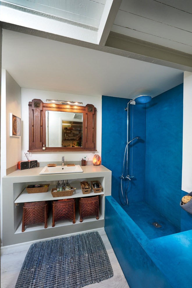 Imagen de cuarto de baño principal mediterráneo de tamaño medio con armarios abiertos, puertas de armario grises, encimera de cemento, encimeras grises, combinación de ducha y bañera, baldosas y/o azulejos azules, paredes blancas y lavabo encastrado
