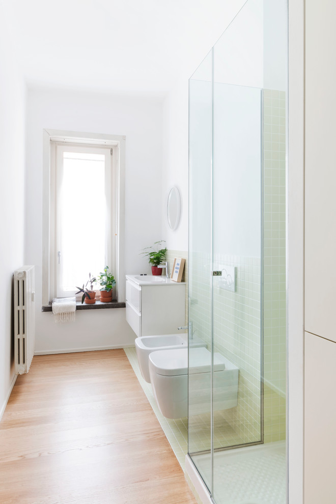Inredning av ett modernt mellanstort badrum med dusch, med släta luckor, vita skåp, en hörndusch, en vägghängd toalettstol, grön kakel, keramikplattor, vita väggar och ljust trägolv