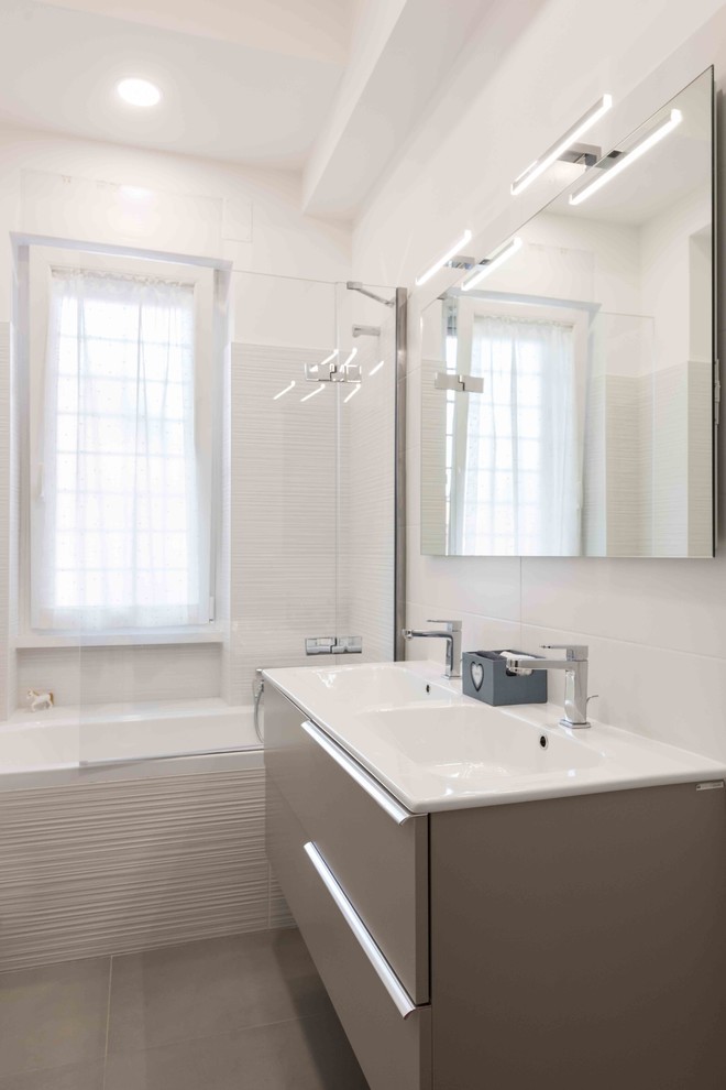 Idéer för funkis en-suite badrum, med ett hörnbadkar, en toalettstol med separat cisternkåpa, vit kakel, porslinskakel, vita väggar, klinkergolv i porslin, ett integrerad handfat och grått golv