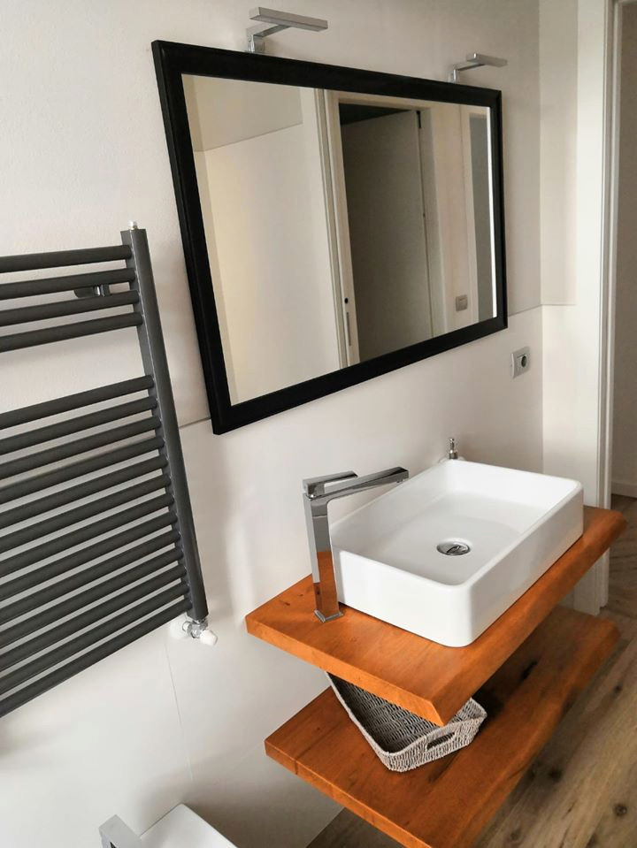 Modern inredning av ett litet en-suite badrum, med öppna hyllor, bruna skåp, ett hörnbadkar, en toalettstol med separat cisternkåpa, vit kakel, vita väggar, klinkergolv i porslin, ett fristående handfat och träbänkskiva