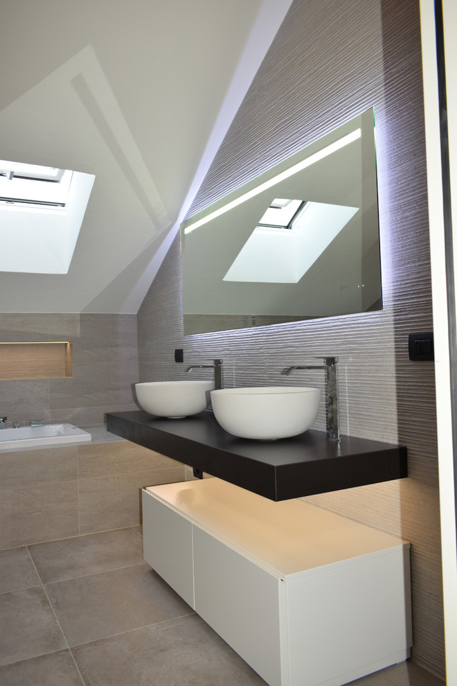 Пример оригинального дизайна: главная ванная комната среднего размера в стиле модернизм с плоскими фасадами, белыми фасадами, гидромассажной ванной, угловым душем, инсталляцией, серой плиткой, керамогранитной плиткой, серыми стенами, полом из керамогранита, настольной раковиной, столешницей из дерева, серым полом, душем с распашными дверями и коричневой столешницей