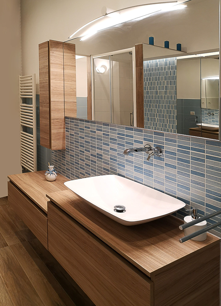 Large danish master blue tile and mosaic tile porcelain tile and brown floor wet room photo in Naples with medium tone wood cabinets, a hot tub, a two-piece toilet, white walls, a vessel sink, wood countertops, a hinged shower door and brown countertops