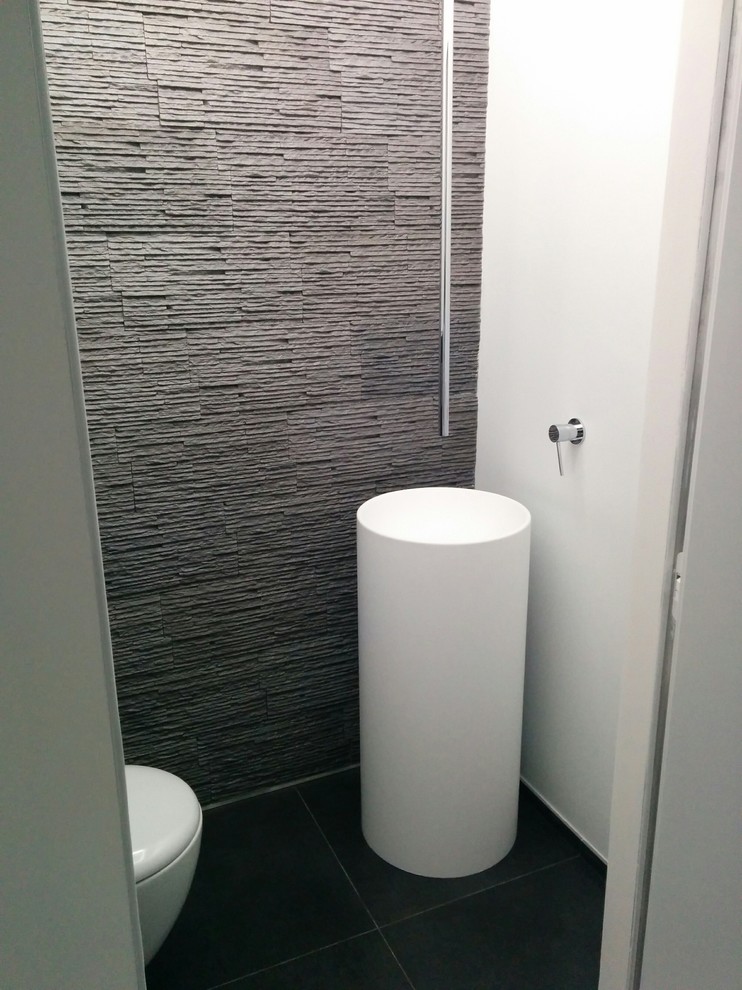 Exempel på ett litet modernt badrum för barn, med en vägghängd toalettstol, cementkakel, vita väggar, klinkergolv i porslin, ett piedestal handfat och grått golv