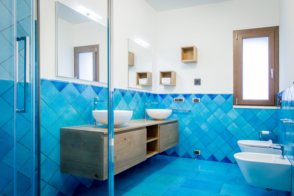 Réalisation d'une salle de bain marine en bois brun avec un placard à porte plane, une douche d'angle, WC suspendus, un mur blanc, une vasque, un plan de toilette en bois, un sol bleu, une cabine de douche à porte battante et un plan de toilette marron.