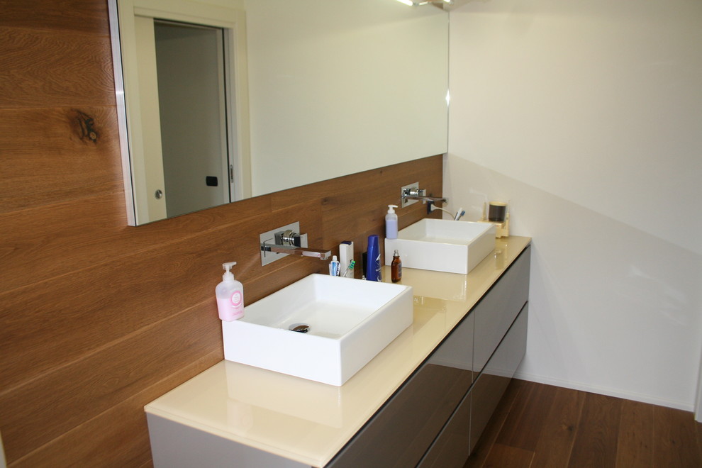 Modern inredning av ett mellanstort badrum med dusch, med släta luckor, bruna skåp, vita väggar, målat trägolv och bänkskiva i glas