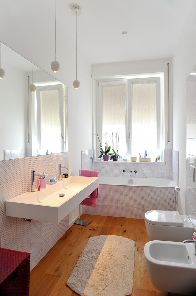 Modern inredning av ett mellanstort badrum, med en vägghängd toalettstol, flerfärgad kakel, keramikplattor, vita väggar, ljust trägolv och ett avlångt handfat