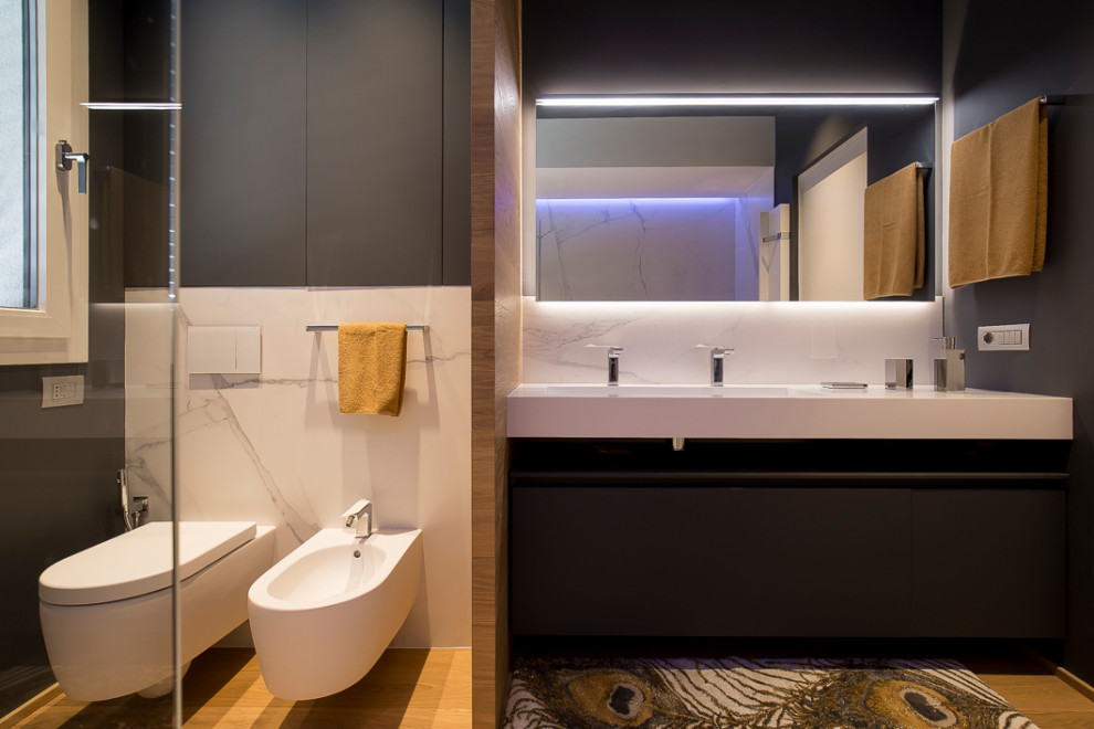 This is an example of a large modern ensuite bathroom in Other with beaded cabinets, grey cabinets, a walk-in shower, a wall mounted toilet, white tiles, grey walls, medium hardwood flooring, an integrated sink, solid surface worktops, brown floors, white worktops, a single sink, a floating vanity unit, a drop ceiling, wainscoting and porcelain tiles.