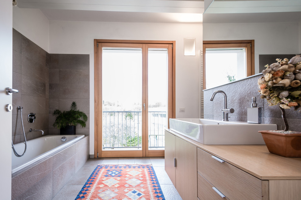 Exempel på ett mellanstort modernt en-suite badrum, med släta luckor, skåp i ljust trä, ett platsbyggt badkar, grå kakel, vita väggar, ett fristående handfat, träbänkskiva och grått golv