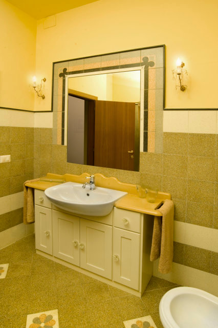 Bild på ett badrum, med flerfärgad kakel, cementkakel, gula väggar, terrazzogolv och ett nedsänkt handfat
