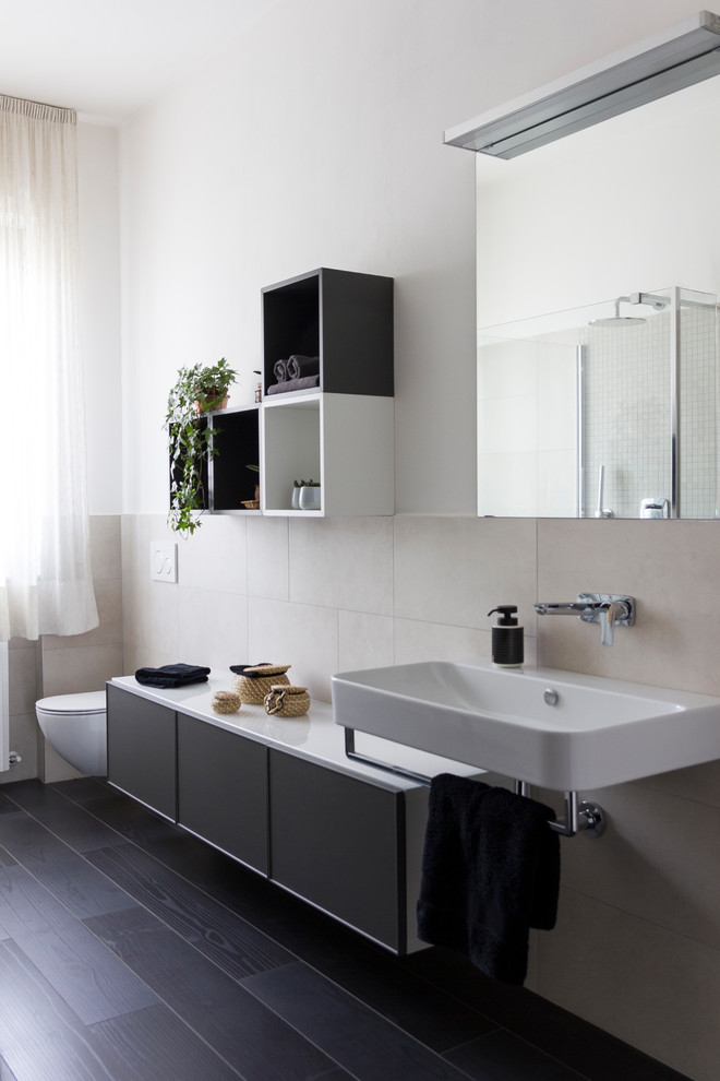 На фото: ванная комната среднего размера в современном стиле с фасадами с утопленной филенкой, серыми фасадами, душем без бортиков, инсталляцией, бежевой плиткой, керамогранитной плиткой, белыми стенами, полом из керамогранита, душевой кабиной, подвесной раковиной, стеклянной столешницей, черным полом, открытым душем и белой столешницей с