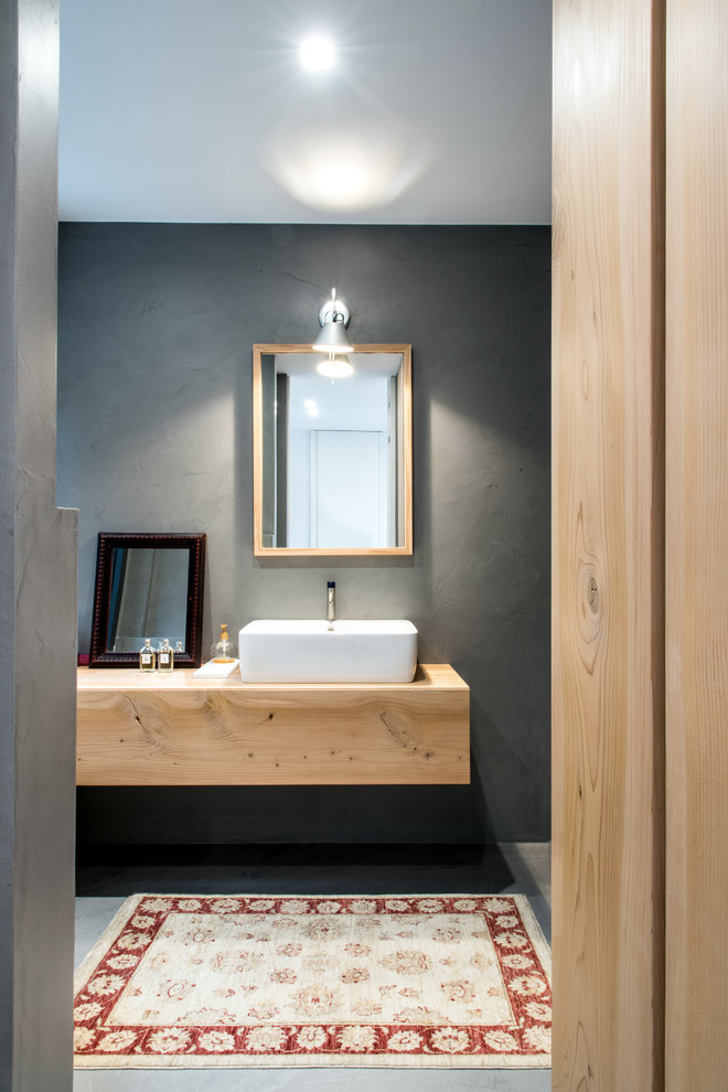 Réalisation d'une salle d'eau urbaine en bois clair de taille moyenne avec une douche à l'italienne, un carrelage gris, un mur gris, sol en béton ciré, une vasque, un plan de toilette en bois et un sol gris.
