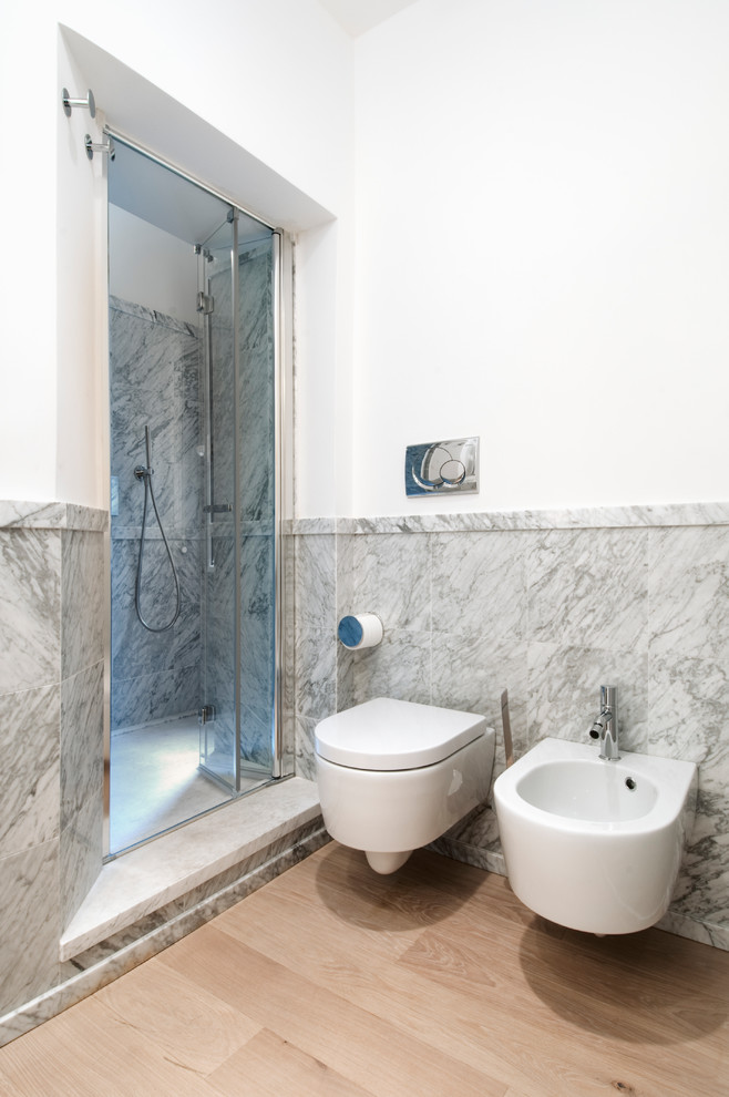 Esempio di una stanza da bagno con doccia contemporanea di medie dimensioni con piastrelle grigie, piastrelle di marmo, parquet chiaro, doccia alcova, WC a due pezzi e porta doccia a battente