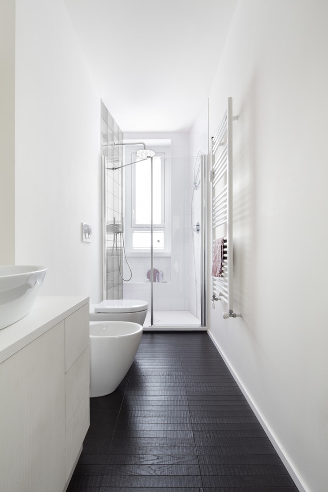 Idée de décoration pour une salle de bain longue et étroite design de taille moyenne avec un placard à porte plane, des portes de placard blanches, un bidet, un mur blanc, parquet peint, une vasque, un sol noir et une cabine de douche à porte battante.