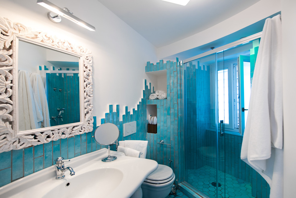 Foto på ett litet maritimt badrum med dusch, med en dusch i en alkov, en toalettstol med hel cisternkåpa, stickkakel, vita väggar, mosaikgolv och ett väggmonterat handfat