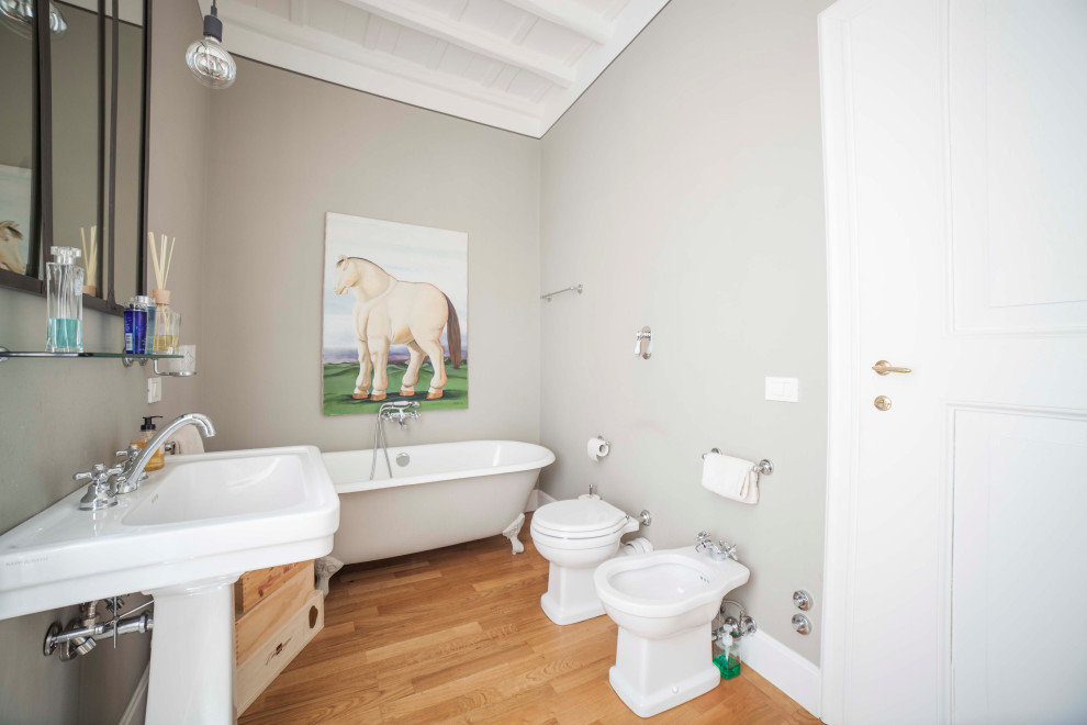 Cette image montre une grande salle de bain principale minimaliste avec une baignoire sur pieds, WC séparés, un carrelage gris, un mur gris, un sol en bois brun, un lavabo de ferme et un sol beige.