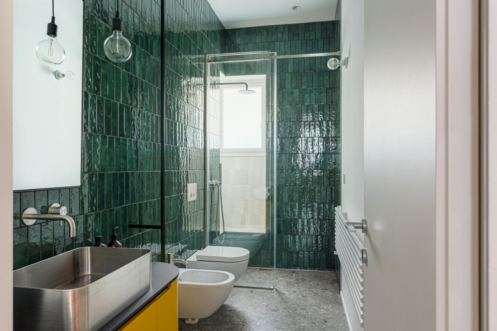 Modelo de cuarto de baño moderno grande con armarios con rebordes decorativos, puertas de armario amarillas, ducha abierta, sanitario de pared, baldosas y/o azulejos verdes, baldosas y/o azulejos de cerámica, paredes verdes, suelo de mármol, aseo y ducha, lavabo sobreencimera, encimera de laminado, suelo gris y encimeras negras