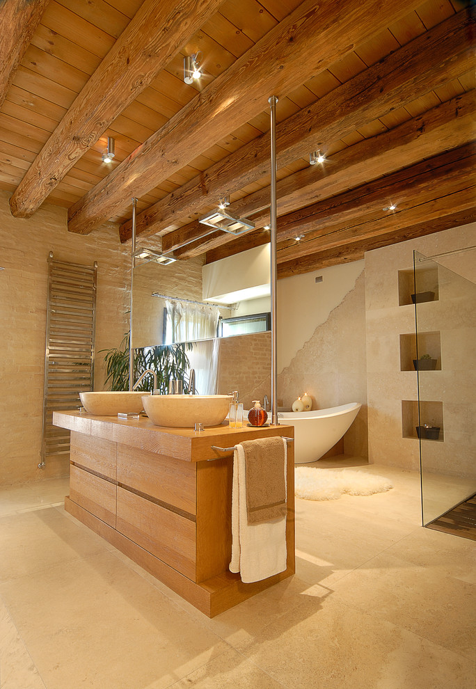 Стильный дизайн: главная ванная комната в современном стиле с настольной раковиной, плоскими фасадами, отдельно стоящей ванной, бежевыми стенами, светлыми деревянными фасадами, душем без бортиков и столешницей из дерева - последний тренд