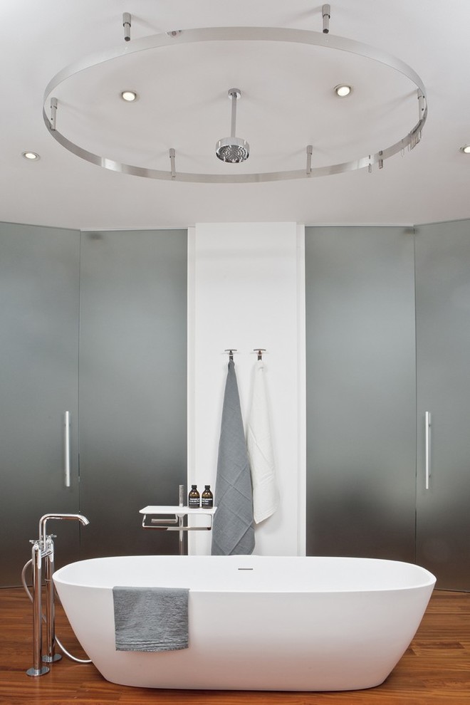 Immagine di una stanza da bagno contemporanea con vasca freestanding, pareti bianche, pavimento in legno massello medio e doccia con tenda