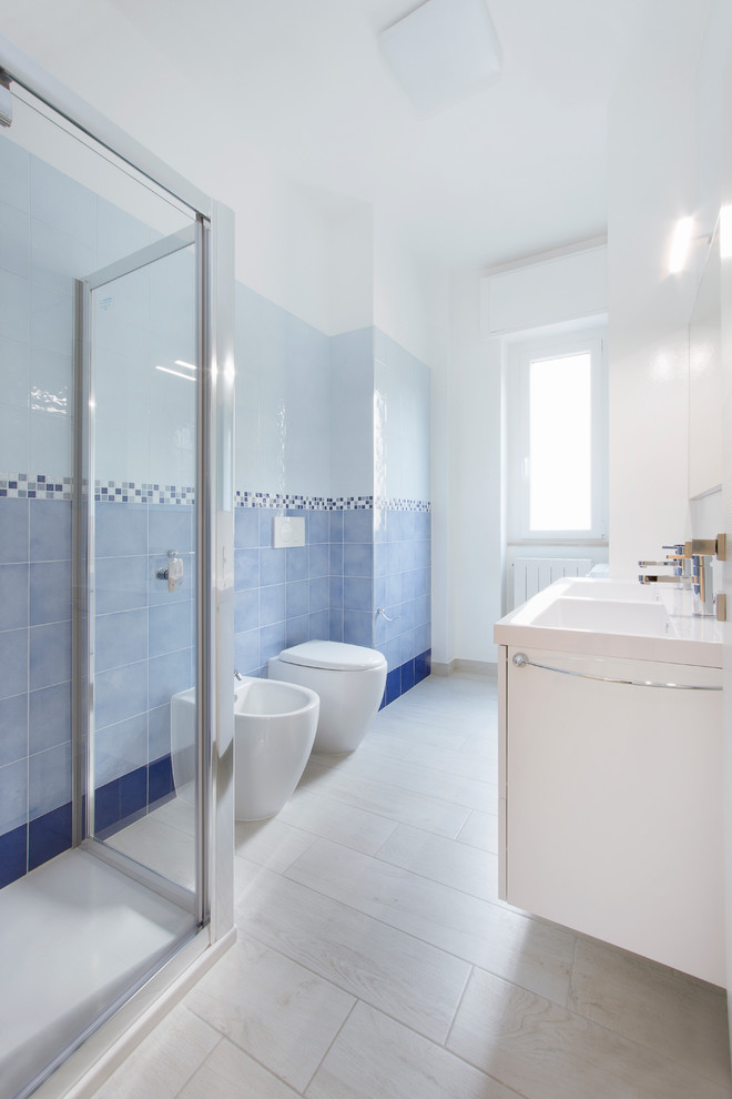 Idée de décoration pour une salle de bain marine avec des portes de placard blanches, une douche d'angle, un bidet, un carrelage bleu et un lavabo intégré.