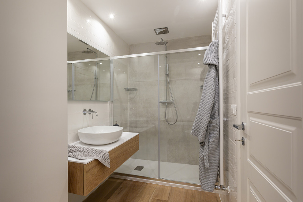 Inspiration for a medium sized modern shower room bathroom in Milan with flat-panel cabinets, light wood cabinets, an alcove shower, a one-piece toilet, white tiles, porcelain tiles, white walls, light hardwood flooring, a vessel sink, a sliding door and white worktops.
