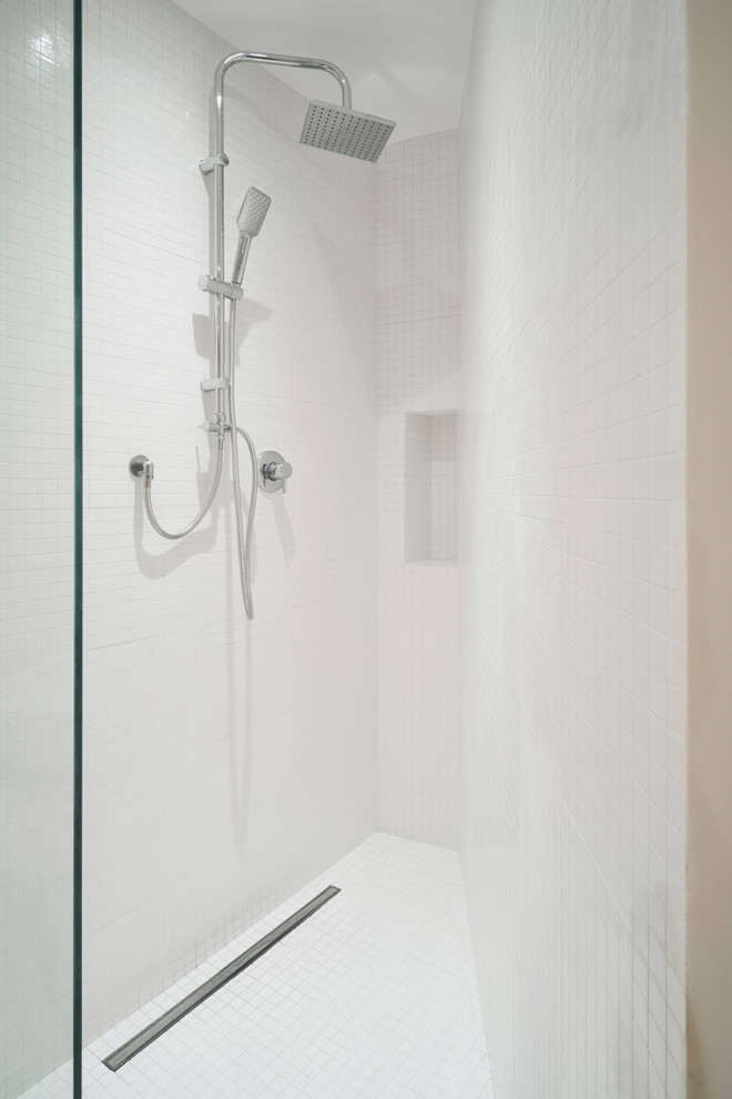 Modern inredning av ett litet badrum med dusch, med öppna hyllor, skåp i ljust trä, en dusch i en alkov, en toalettstol med separat cisternkåpa, vit kakel, porslinskakel, vita väggar, bambugolv, ett fristående handfat, träbänkskiva, brunt golv och med dusch som är öppen