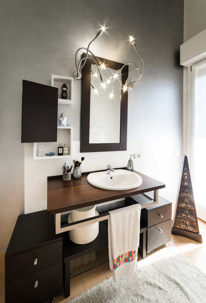 Medium sized industrial ensuite bathroom in Milan with flat-panel cabinets, dark wood cabinets, a built-in bath, a two-piece toilet, beige tiles, ceramic tiles, multi-coloured walls, ceramic flooring, a built-in sink, wooden worktops and beige floors.