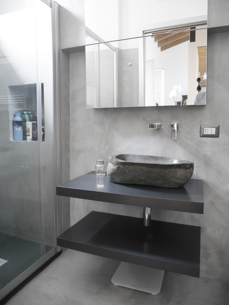 Bild på ett mellanstort funkis grå grått badrum med dusch, med en dusch i en alkov, grå kakel, grå väggar, betonggolv, ett fristående handfat, grått golv, dusch med skjutdörr och öppna hyllor