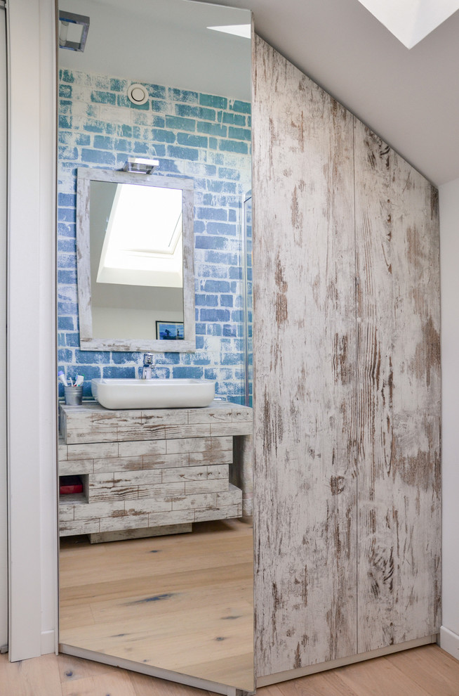 Shabby chic-inspirerad inredning av ett litet badrum med dusch, med släta luckor, skåp i ljust trä, en hörndusch, en vägghängd toalettstol, blå väggar, ljust trägolv, ett fristående handfat och laminatbänkskiva