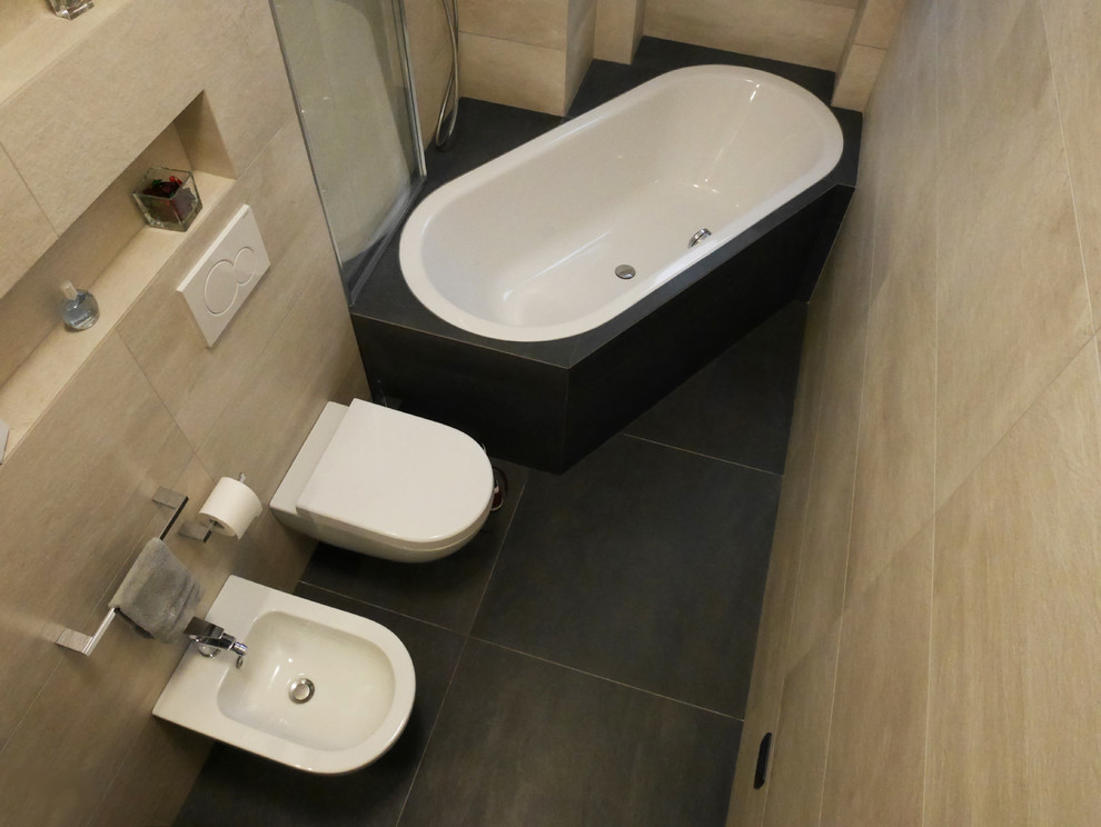 Modern inredning av ett mellanstort en-suite badrum, med släta luckor, grå skåp, ett platsbyggt badkar, en dusch/badkar-kombination, en vägghängd toalettstol, beige kakel, porslinskakel, beige väggar, klinkergolv i porslin, ett integrerad handfat, svart golv och dusch med gångjärnsdörr