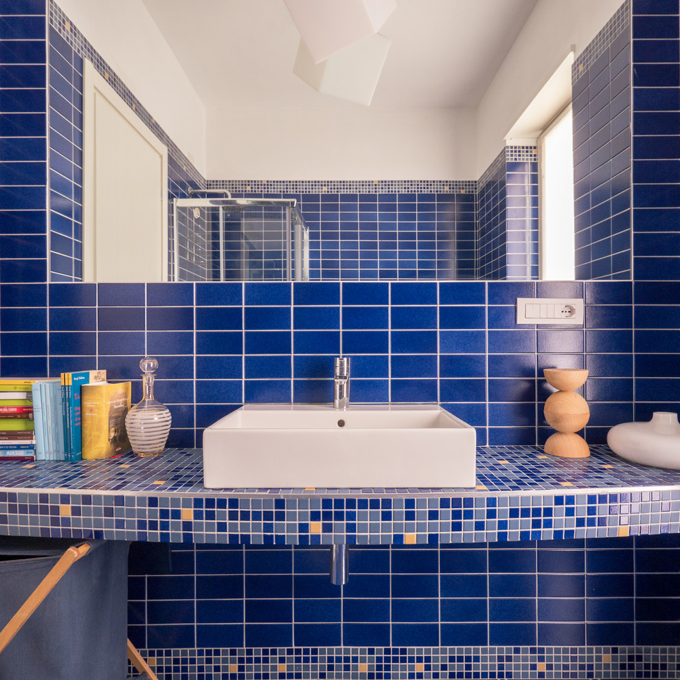 Inredning av ett modernt litet badrum med dusch, med en hörndusch, en toalettstol med separat cisternkåpa, blå kakel, mosaik, blå väggar, klinkergolv i keramik, ett avlångt handfat, bänkskiva i betong, blått golv och dusch med skjutdörr